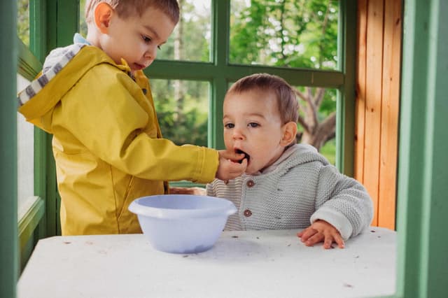 toddler boy feeding his little sibling with berries
